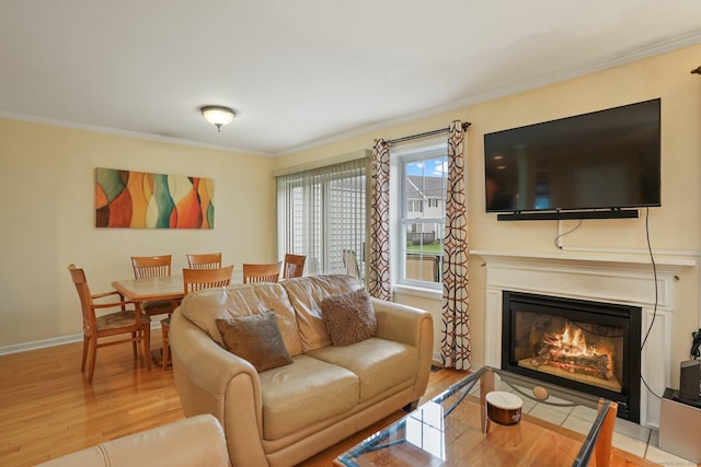 living room featuring a glass covered fireplace, ornamental molding, baseboards, and wood finished floors