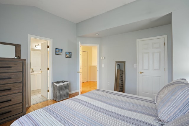 bedroom with light wood-type flooring, connected bathroom, and vaulted ceiling