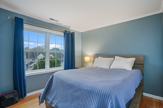 bedroom with visible vents, crown molding, baseboards, and wood finished floors