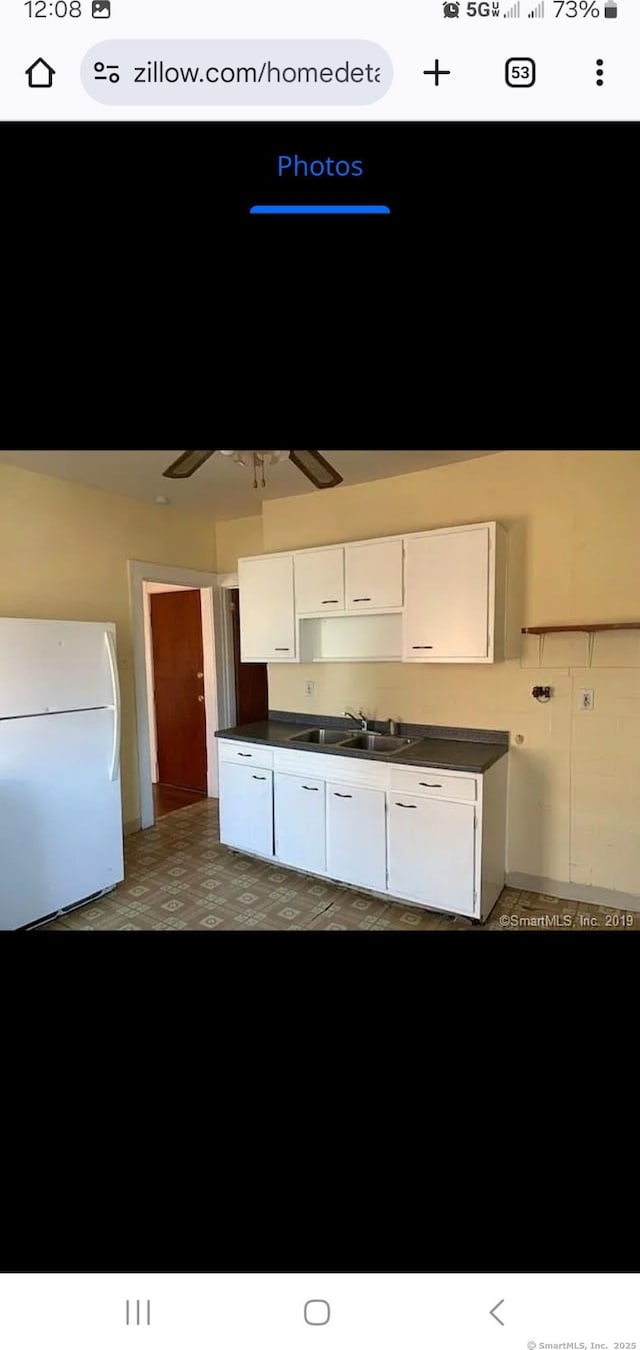 kitchen with a sink, dark countertops, white cabinets, and freestanding refrigerator