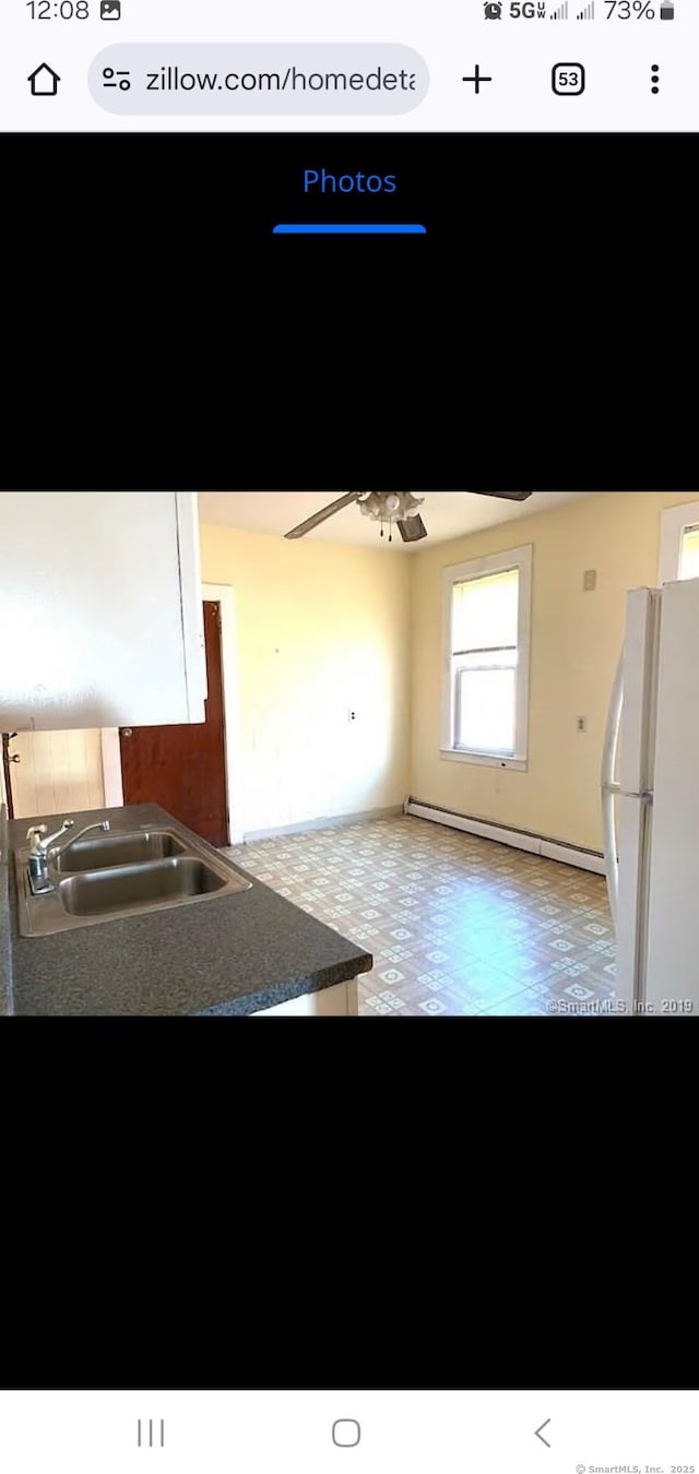 kitchen with a ceiling fan, a sink, dark countertops, freestanding refrigerator, and baseboard heating