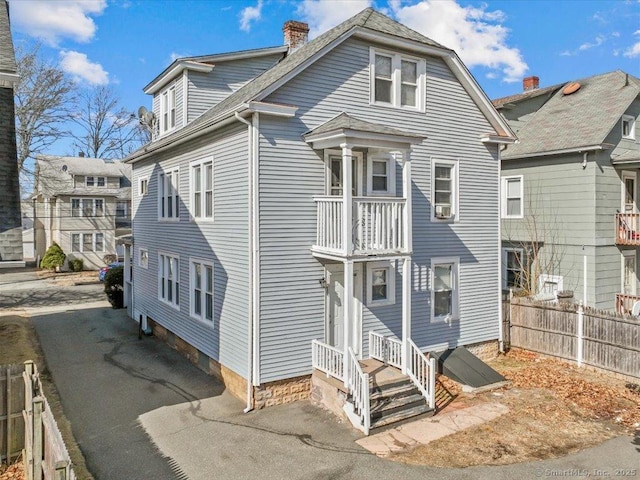 view of front of home with aphalt driveway, a chimney, a balcony, and fence