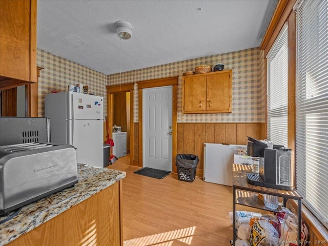 kitchen featuring a wainscoted wall, light wood finished floors, freestanding refrigerator, and wallpapered walls