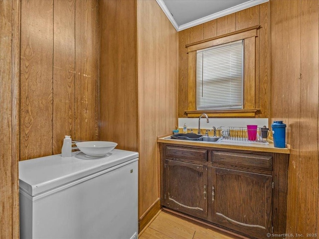 laundry room with a sink, light wood-type flooring, wooden walls, and ornamental molding