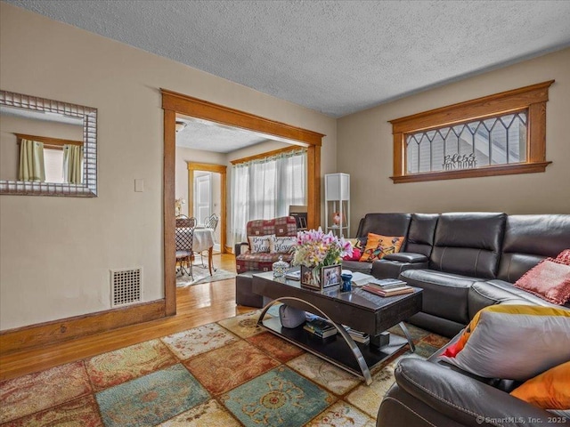 living area featuring visible vents, a textured ceiling, baseboards, and wood finished floors