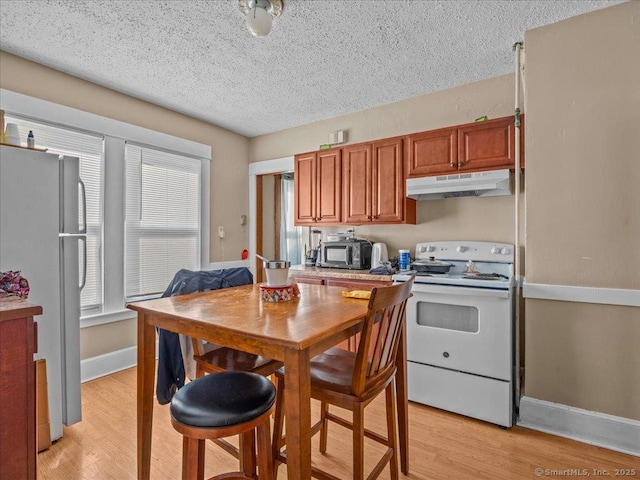 kitchen featuring white appliances, baseboards, under cabinet range hood, a textured ceiling, and light wood-type flooring