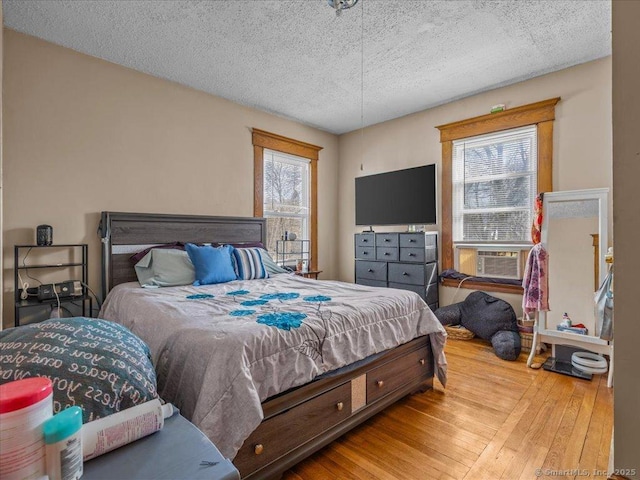 bedroom with cooling unit, a textured ceiling, and hardwood / wood-style flooring