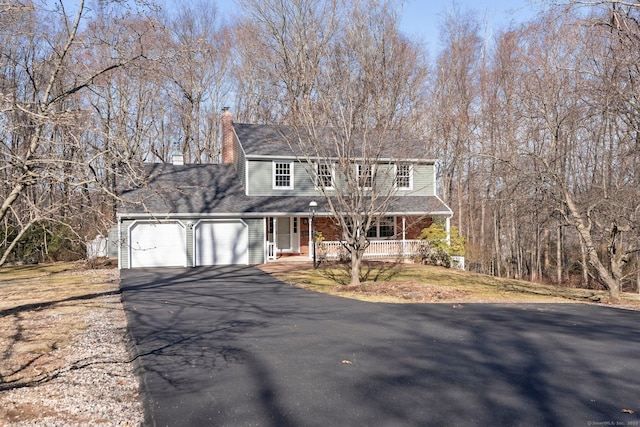 view of front facade with aphalt driveway, covered porch, an attached garage, and a chimney