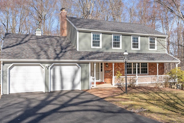 view of front facade featuring a shingled roof, covered porch, a chimney, driveway, and an attached garage