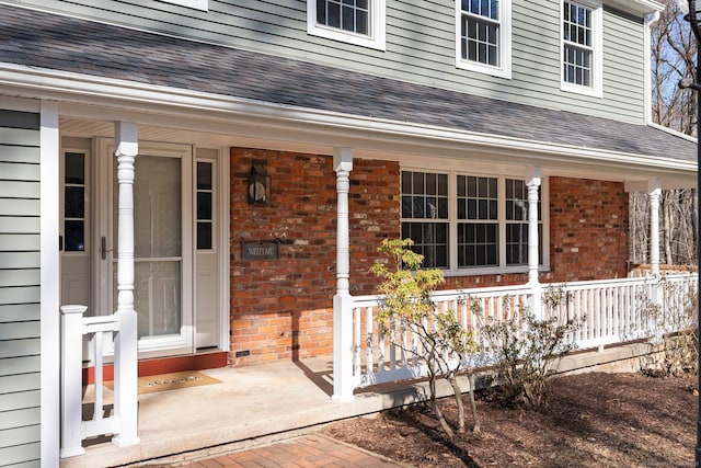 entrance to property featuring brick siding, a porch, and roof with shingles