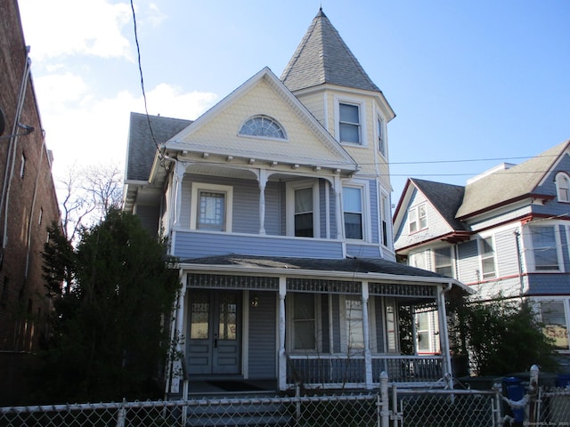 victorian-style house featuring a fenced front yard, covered porch, and a shingled roof