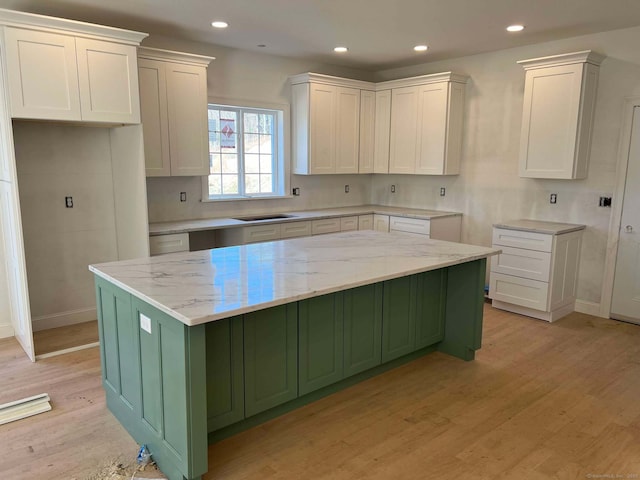kitchen with light wood-type flooring, baseboards, a kitchen island, light stone countertops, and green cabinetry