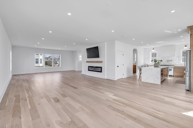 unfurnished living room with recessed lighting, arched walkways, light wood-style floors, and a glass covered fireplace