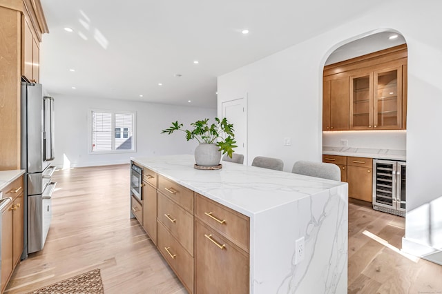 kitchen featuring light stone counters, a center island, wine cooler, light wood-style floors, and appliances with stainless steel finishes