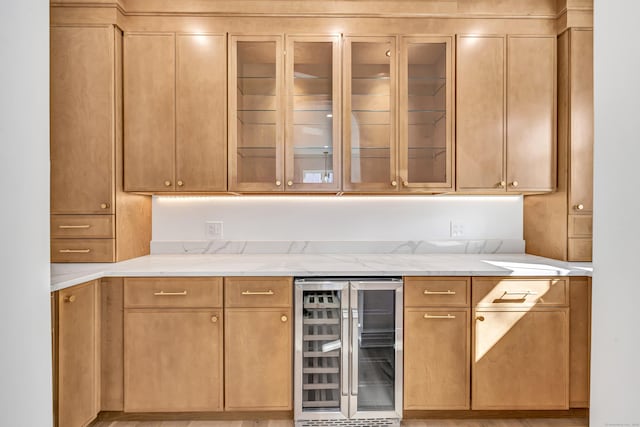 kitchen featuring beverage cooler, glass insert cabinets, and light stone countertops