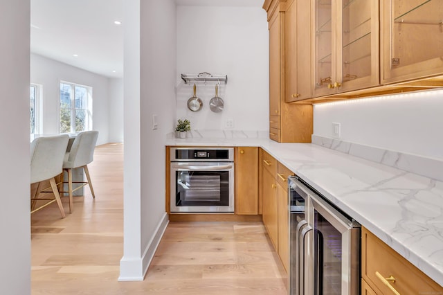 kitchen featuring oven, light wood-type flooring, light stone counters, wine cooler, and glass insert cabinets