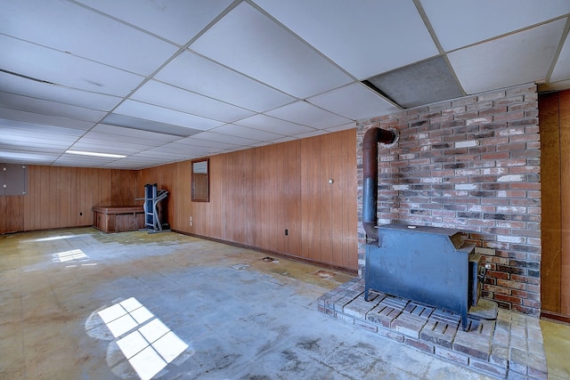 finished basement with a drop ceiling, wood walls, and a wood stove