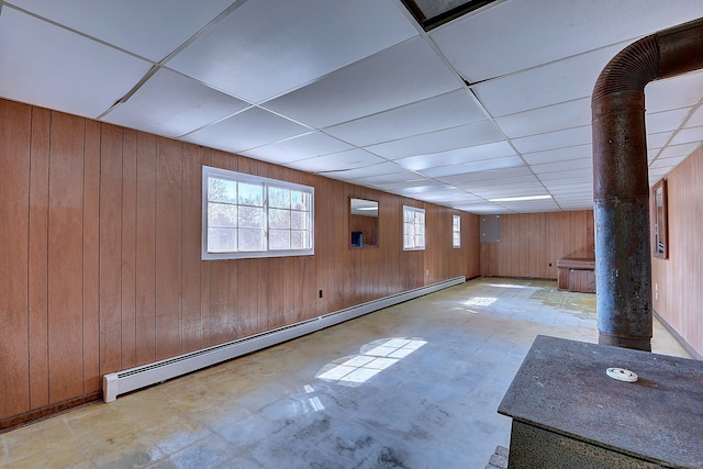 below grade area featuring a drop ceiling, a baseboard heating unit, and wooden walls