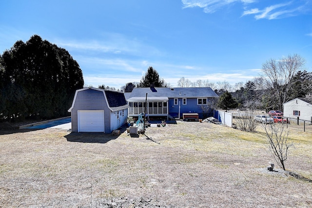 rear view of property featuring a detached garage, fence, a gambrel roof, an outdoor structure, and a sunroom