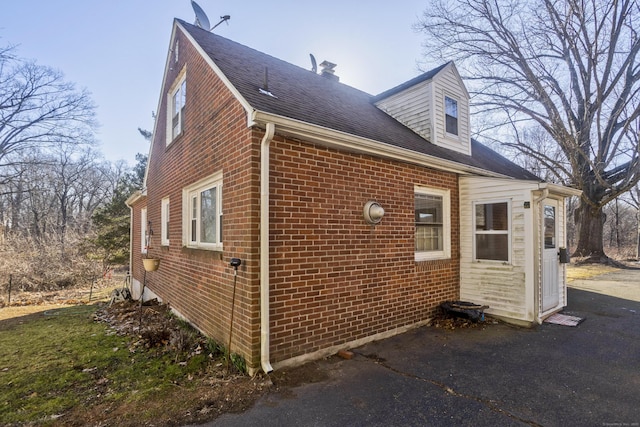 view of property exterior with brick siding and a shingled roof