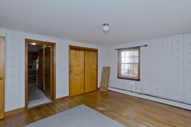 unfurnished bedroom with connected bathroom, baseboards, wood finished floors, a closet, and a baseboard radiator