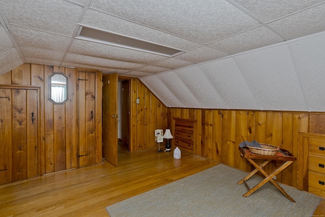 bonus room with vaulted ceiling, wooden walls, and wood finished floors