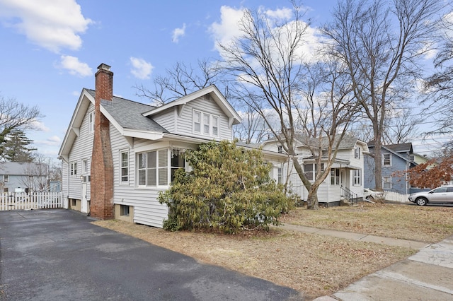 view of front facade with fence, a shingled roof, entry steps, a chimney, and aphalt driveway
