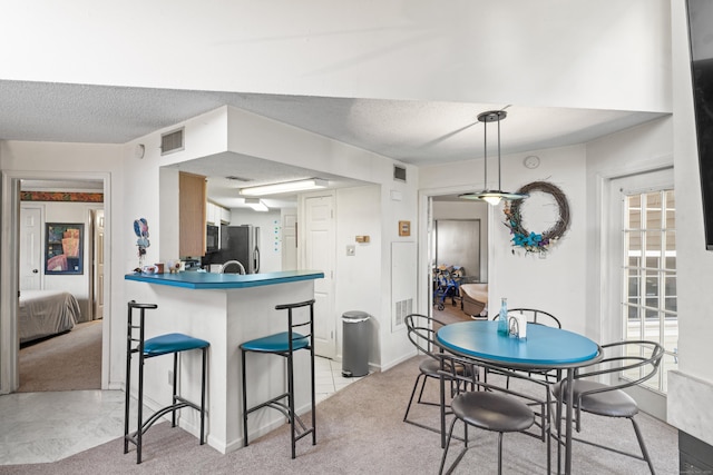 kitchen featuring visible vents, a breakfast bar, stainless steel fridge, a peninsula, and light colored carpet