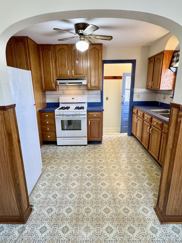 kitchen featuring dark countertops, ventilation hood, white appliances, brown cabinetry, and ceiling fan