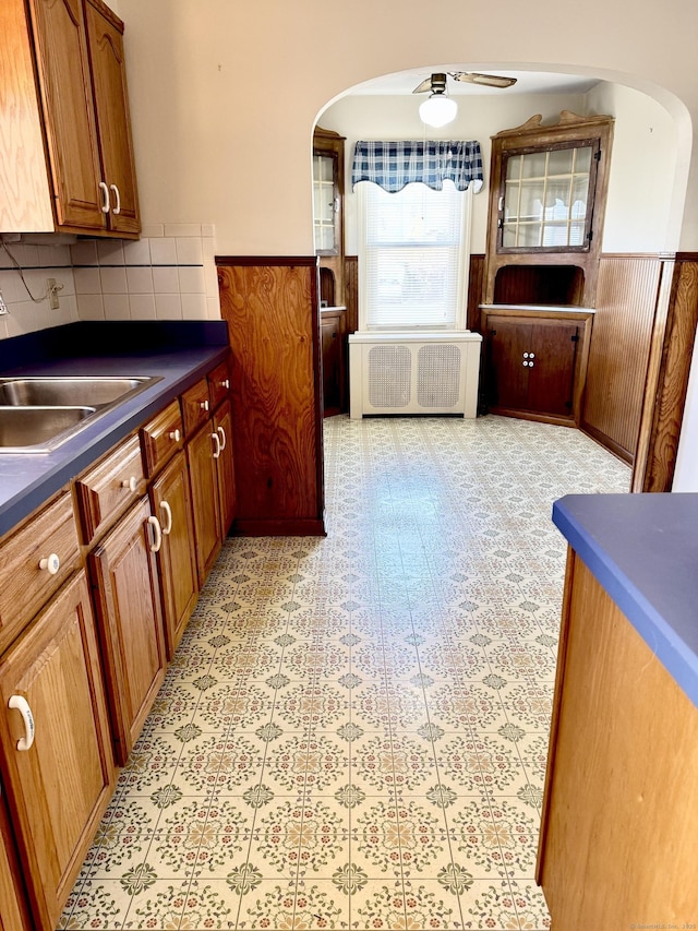 kitchen featuring a sink, dark countertops, arched walkways, radiator, and wainscoting