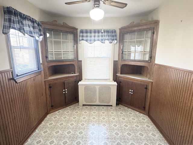 sitting room featuring a wainscoted wall, radiator, wood walls, light floors, and ceiling fan