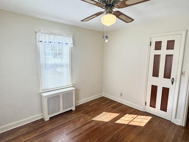 empty room with radiator heating unit, a ceiling fan, dark wood-style flooring, and baseboards