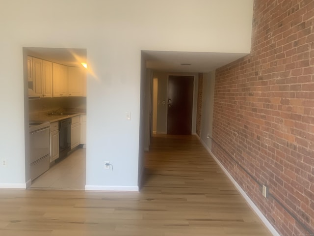 hallway with baseboards, light wood-style floors, and brick wall