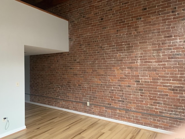 empty room featuring wood finished floors, baseboards, and brick wall