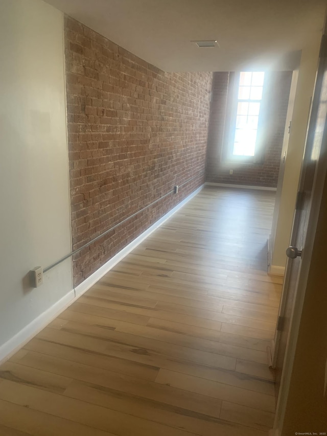 unfurnished room featuring light wood-style floors, baseboards, and brick wall