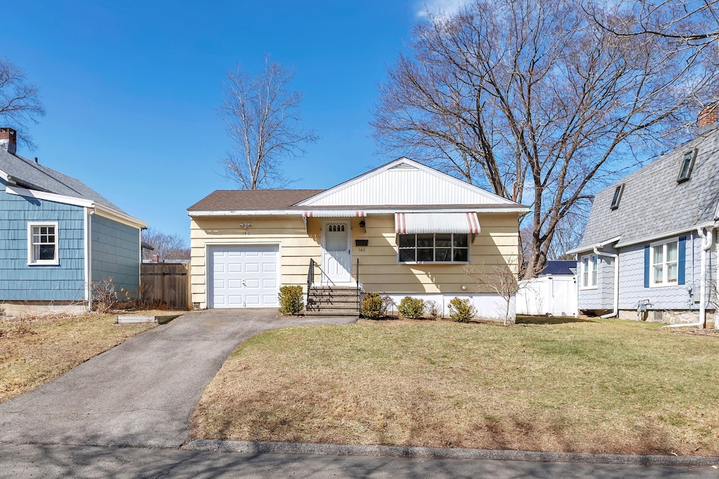 view of front of home with aphalt driveway, fence, a garage, and a front lawn