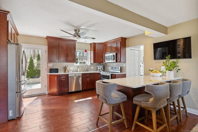 kitchen with a breakfast bar area, dark wood-style flooring, a sink, decorative backsplash, and stainless steel appliances