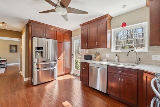 kitchen with a sink, stainless steel appliances, decorative backsplash, ceiling fan, and dark wood-style flooring