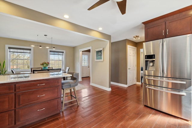 kitchen featuring stainless steel fridge with ice dispenser, dark wood finished floors, light countertops, a kitchen bar, and a ceiling fan