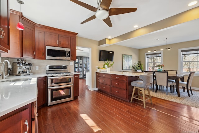 kitchen featuring a ceiling fan, a sink, stainless steel appliances, light countertops, and dark wood-type flooring