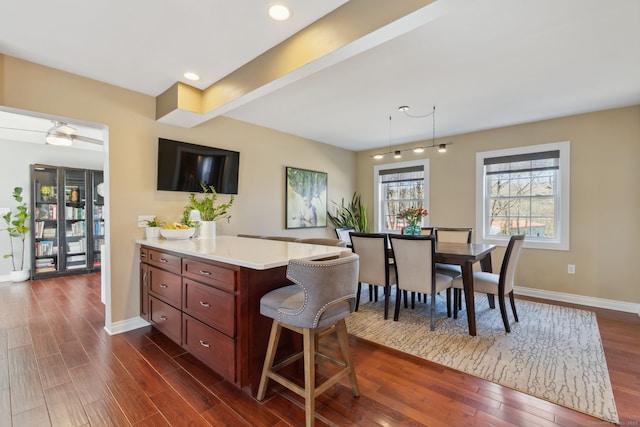 kitchen with baseboards, dark wood finished floors, recessed lighting, light countertops, and a kitchen bar