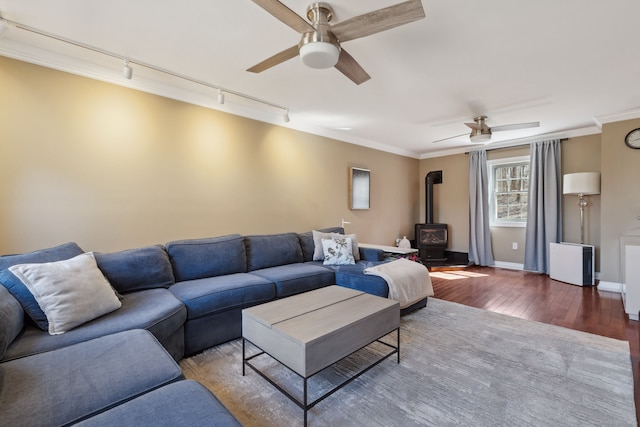 living area featuring wood-type flooring, ceiling fan, a wood stove, and ornamental molding