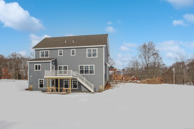 snow covered back of property with a deck and stairs