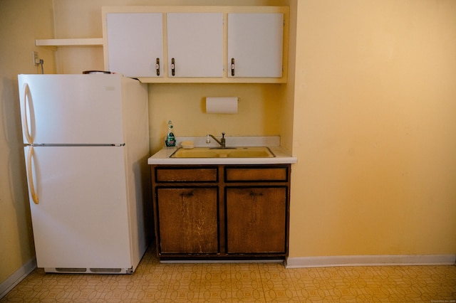 kitchen featuring baseboards, light countertops, freestanding refrigerator, white cabinets, and a sink