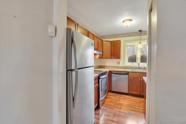 827 Oronoke Rd Apt 2-11, Waterbury, CT 06708 - kitchen featuring light wood finished floors, stainless steel appliances, brown cabinetry, a textured ceiling, and a sink