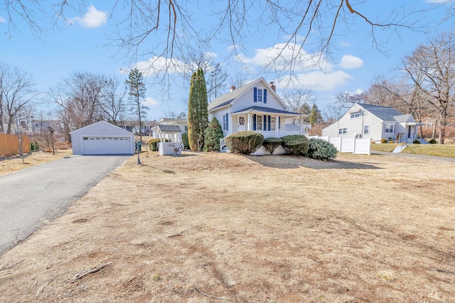 view of front of home with a detached garage, fence, covered porch, a chimney, and an outbuilding