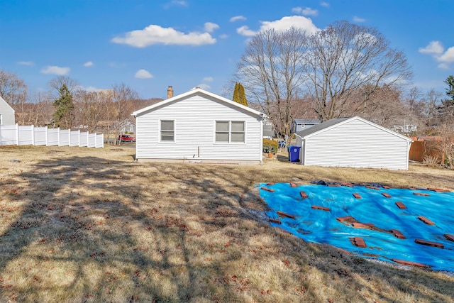 rear view of property featuring a yard, an outbuilding, a chimney, and fence