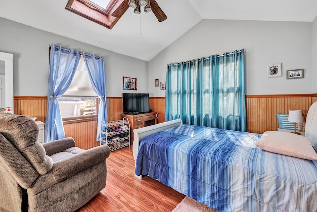 bedroom with ceiling fan, lofted ceiling with skylight, a wainscoted wall, wood walls, and wood finished floors