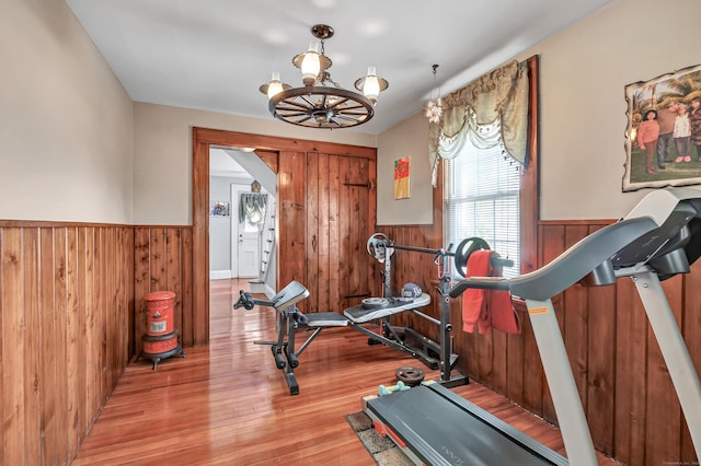 workout room with a chandelier, wooden walls, wainscoting, and wood finished floors