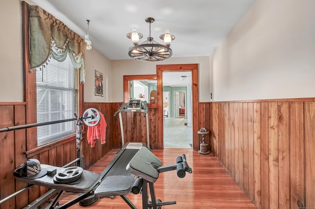 exercise area with wood finished floors, a notable chandelier, wood walls, and wainscoting